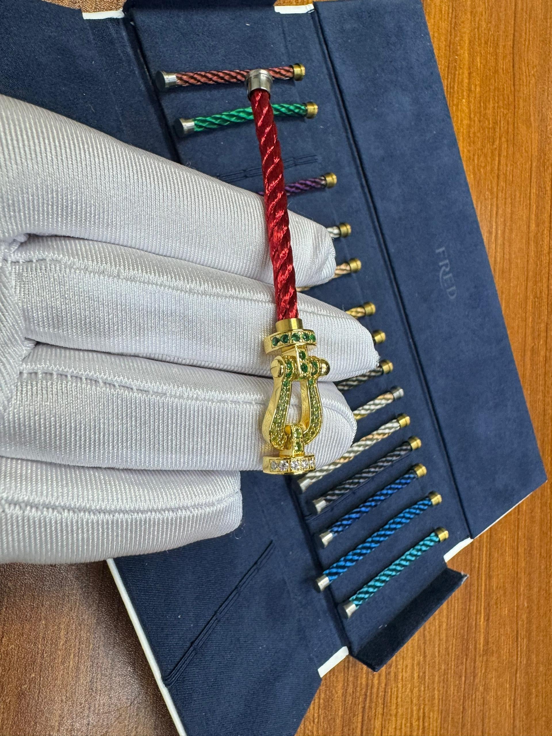 צמיד יוקרתי עם רצועת חבל אדומה ואבזם בגוון זהב משובץ זירקונים ירוקים נוצצים