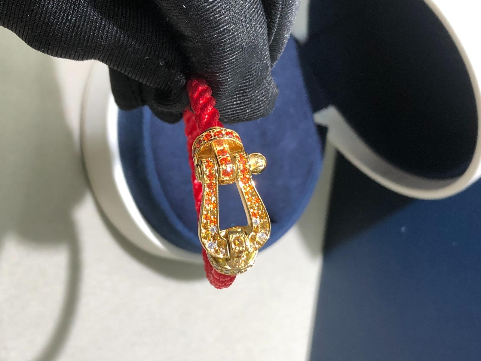 צמיד יוקרתי יוקרתי עם רצועת חבל (עבה) אדום,הבזם בעיצוב רולאן גארוס. בציפוי זהב צהוב, 18 קראט משובץ בזירקונים כתומים אדומים ולבנים - Jewelluxe