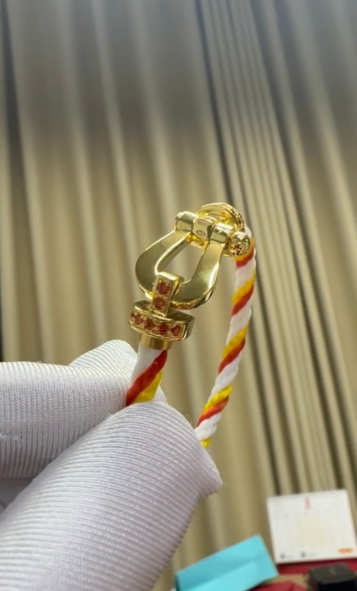 צמיד יוקרתי עם רצועת חבל בגווני כתום, לבן וצהוב ואבזם בגוון זהב משובץ בזירקונים כתומים