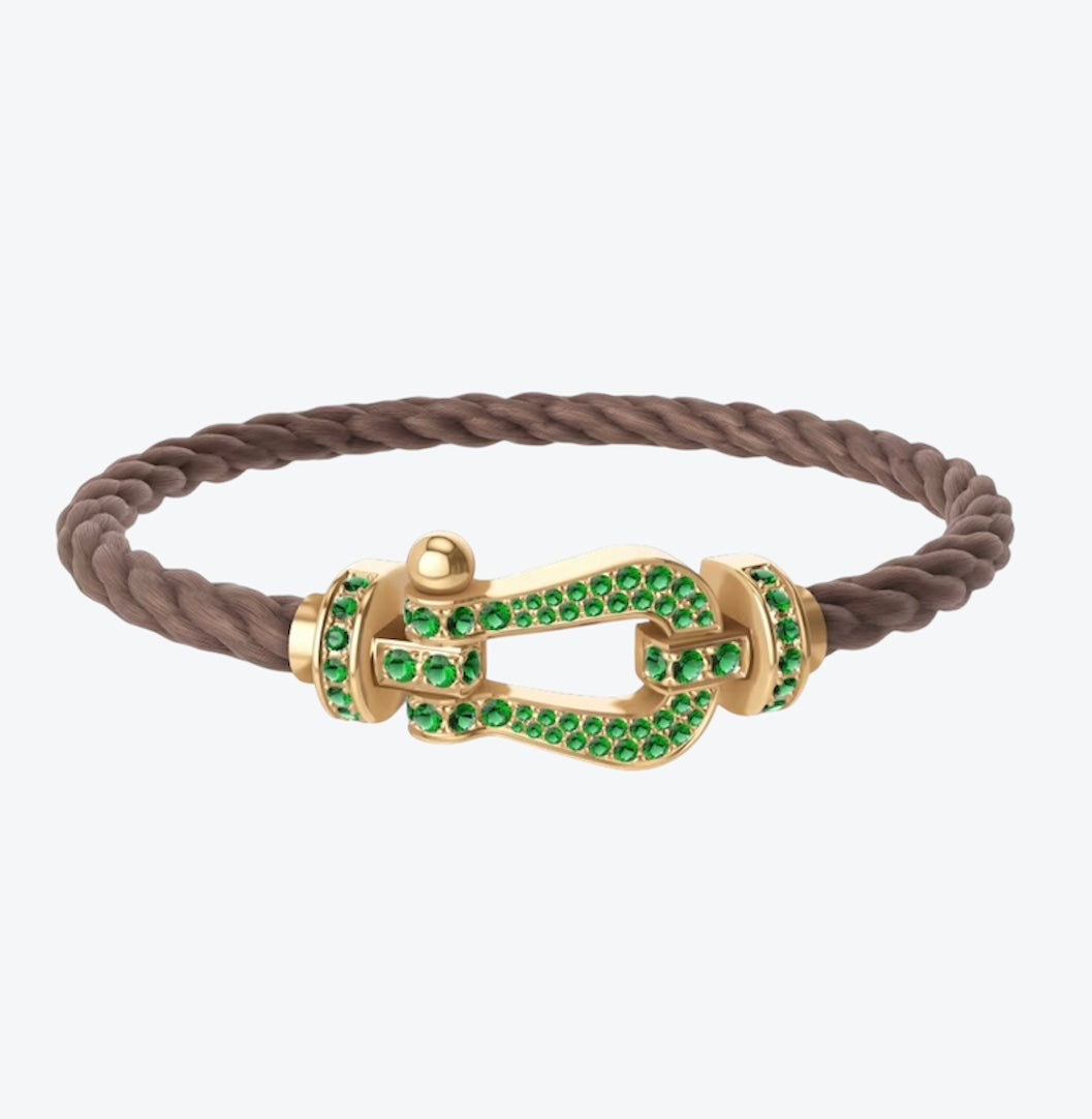 צמיד יוקרתי עם רצועת חבל חומה ואבזם בגוון זהב משובץ זירקונים ירוקים נוצצים