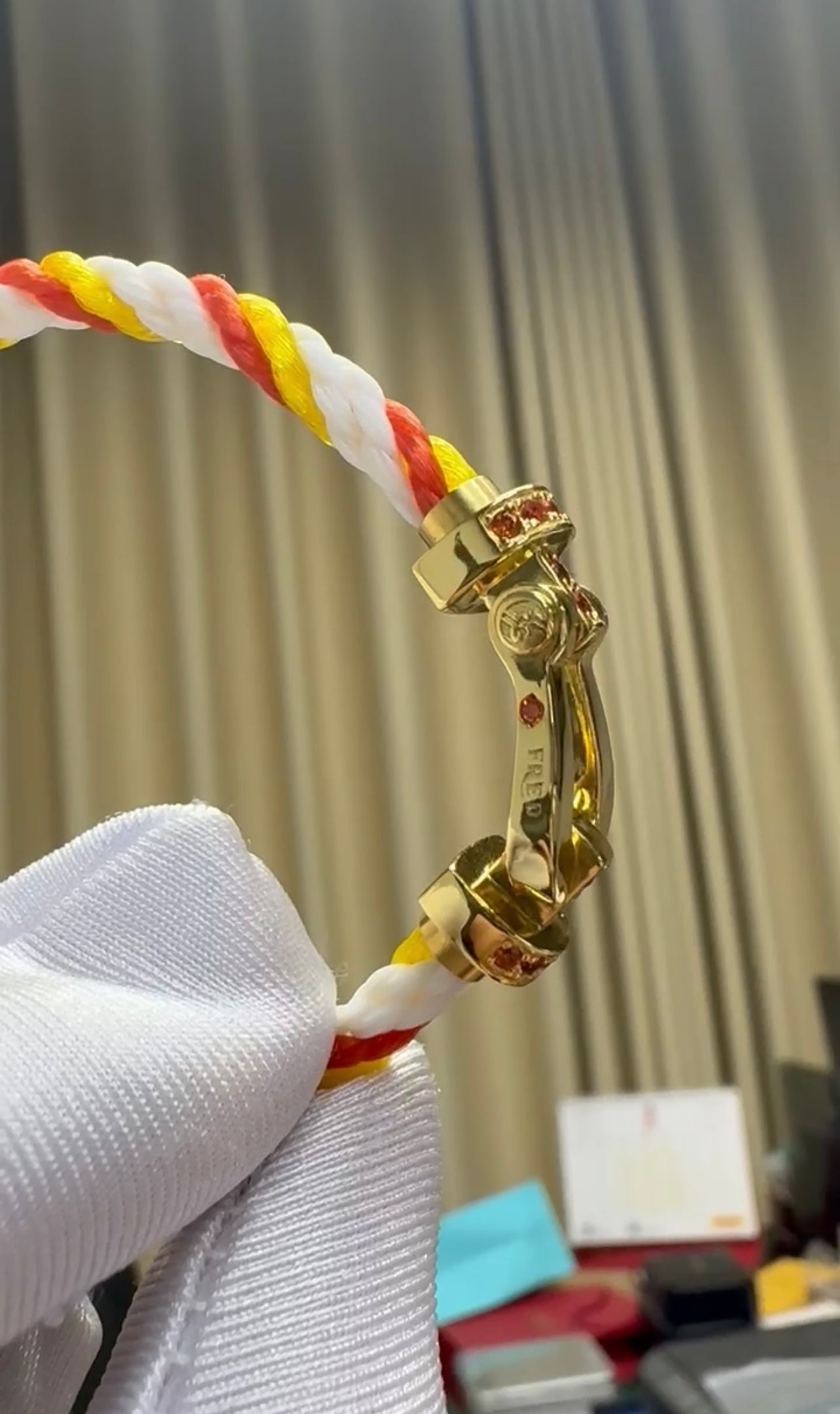 צמיד יוקרתי עם רצועת חבל בגווני כתום, לבן וצהוב ואבזם בגוון זהב משובץ בזירקונים כתומים