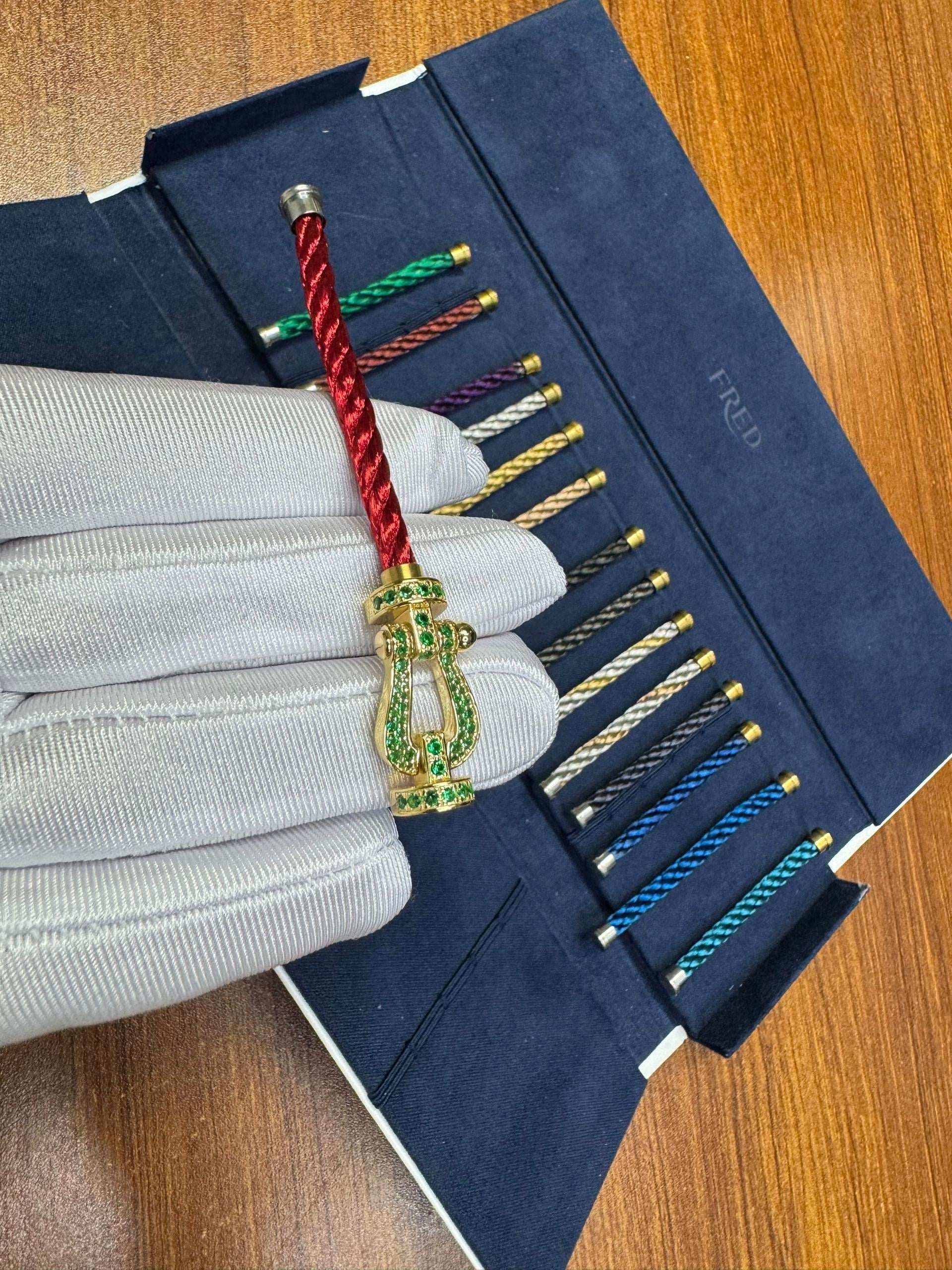 צמיד יוקרתי עם רצועת חבל אדומה ואבזם בגוון זהב משובץ זירקונים ירוקים נוצצים