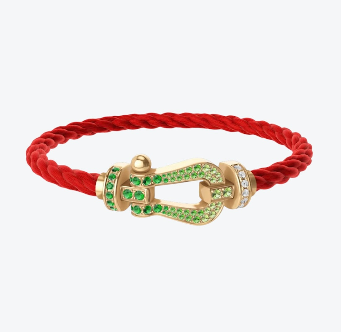 צמיד יוקרתי עם רצועת חבל אדומה ואבזם בגוון זהב משובץ זירקונים ירוקים נוצצים